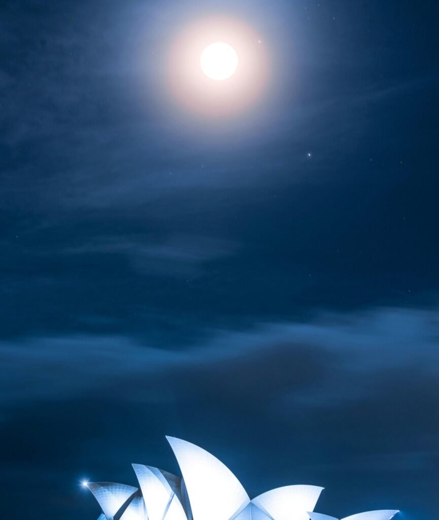 Stunning view of the Sydney Opera House illuminated under a bright moonlit sky at night.